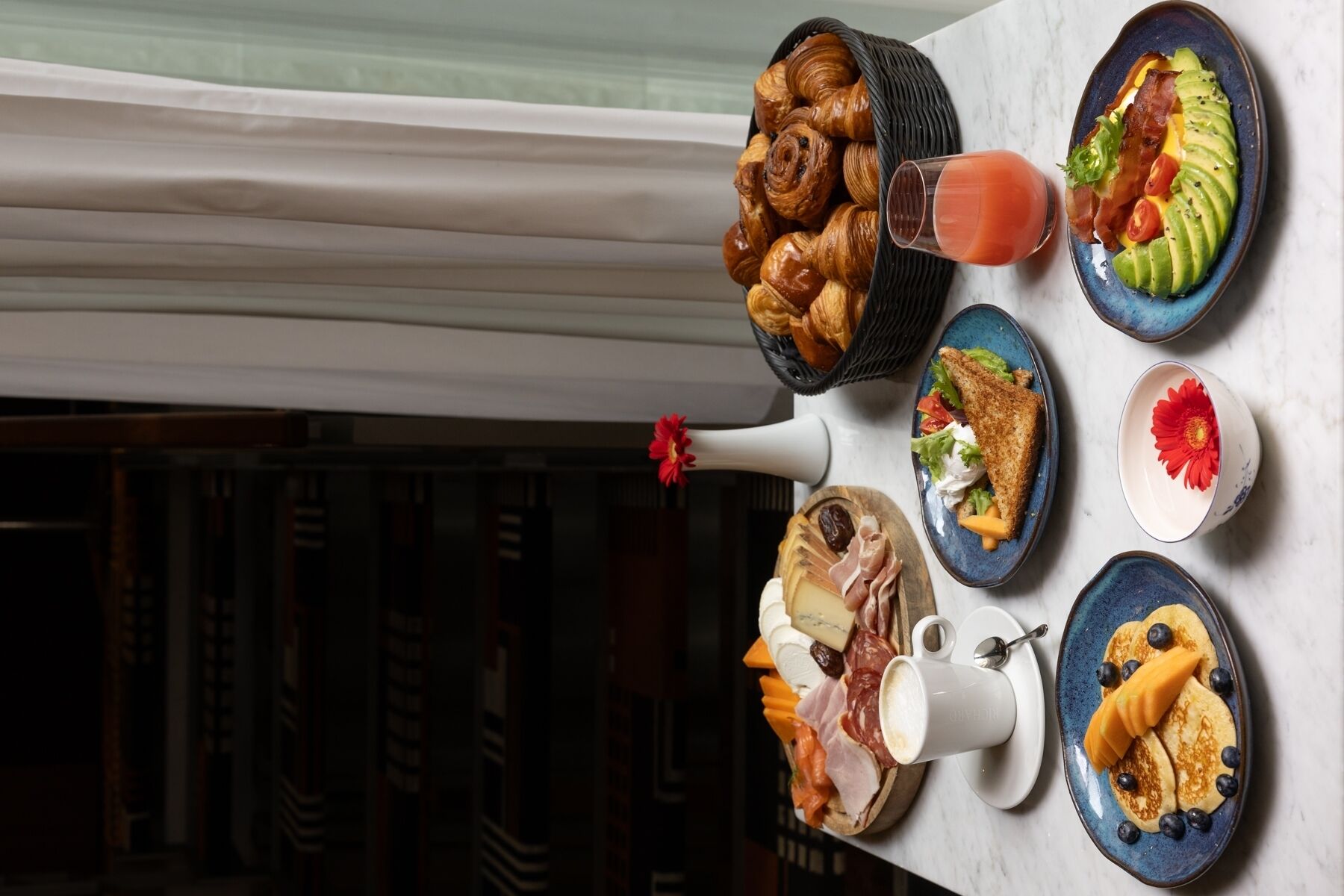 A table with various breakfast items including croissants, a salad, pancakes, and a cheese platter.