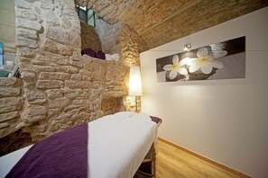 A stone-walled room with a bed, a wall-mounted lamp, and a framed picture of a flower. - Hotel Le Place d'Armes - Relais & Châteaux (Luxembourg City)