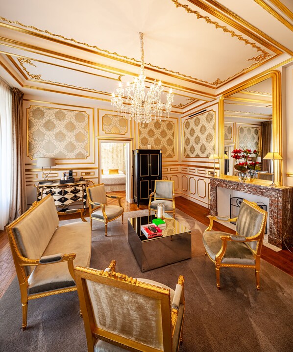 A luxurious living room with ornate gold detailing, a chandelier, and a large mirror.