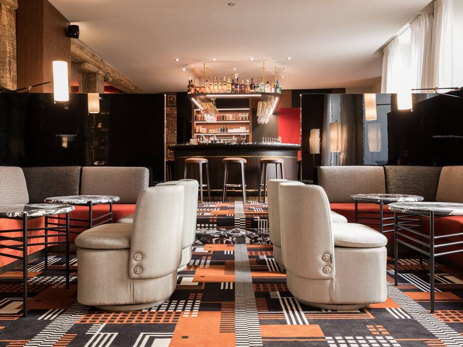 A bar area with stools and a bar counter, a patterned carpet, and a modern interior design.