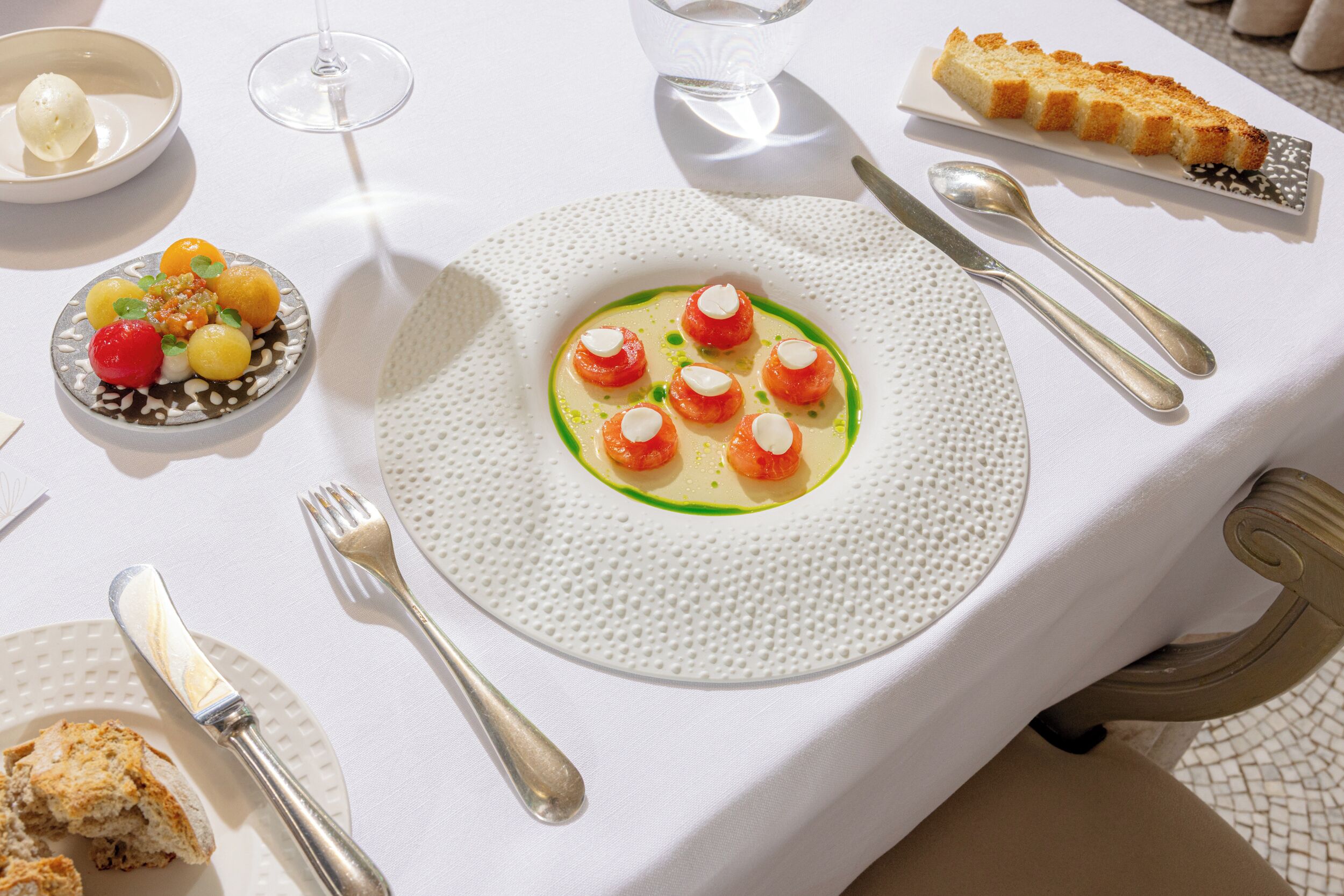 A dining table with a white tablecloth, a plate of food, cutlery, and a glass of water.