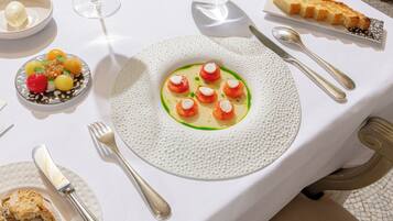 A dining table with a white tablecloth, a plate of food, cutlery, and a glass of water.