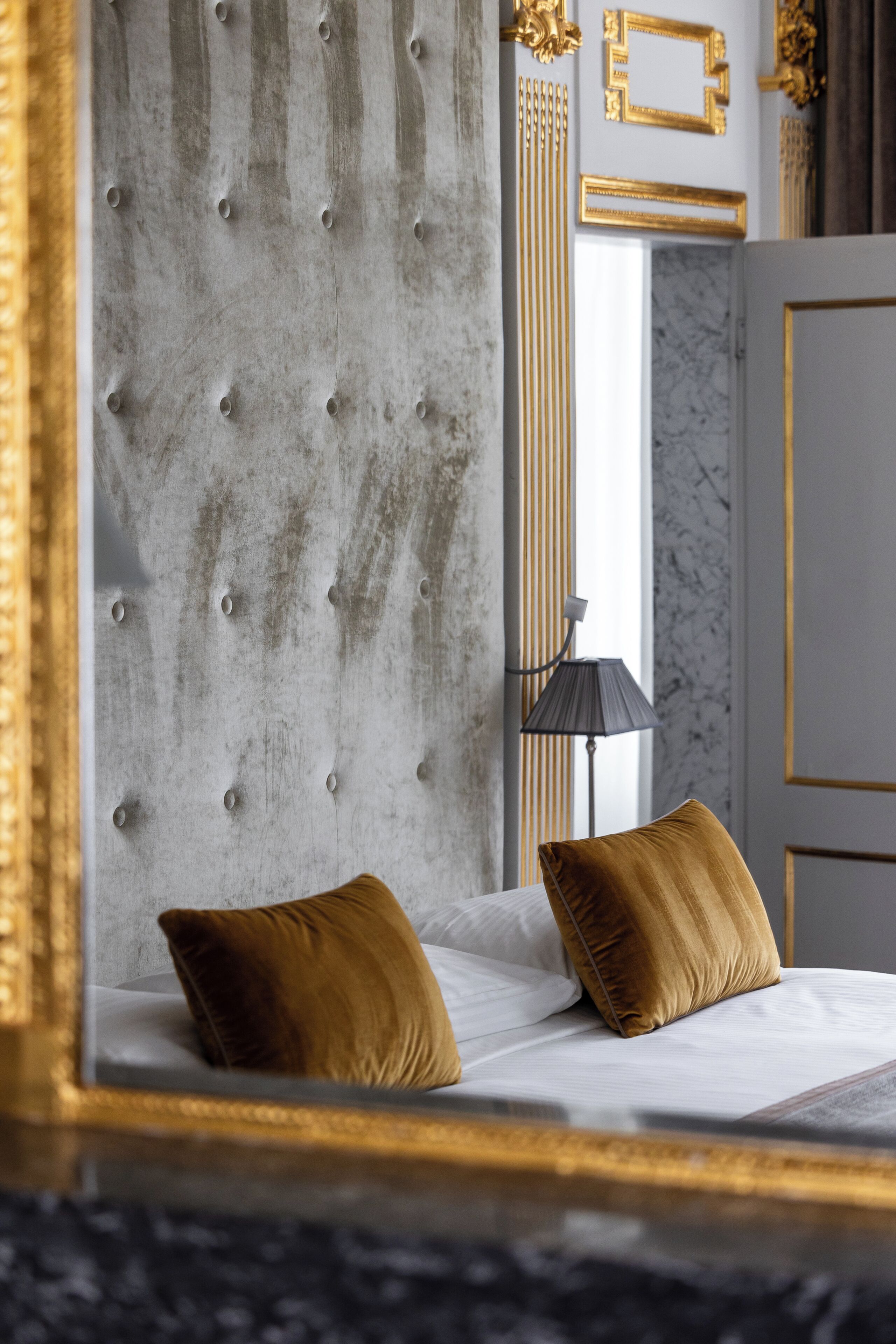 A bedroom with a tufted headboard, a bed with two pillows, a lamp, and a marble wall.