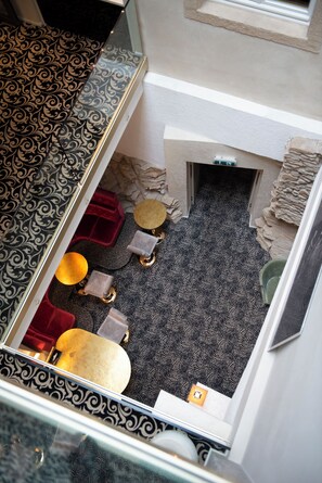 A view from a window overlooking a room with patterned carpet, a red chair, a round table, and a small stool. - Hotel Le Place d'Armes - Relais & Châteaux (Luxembourg City)