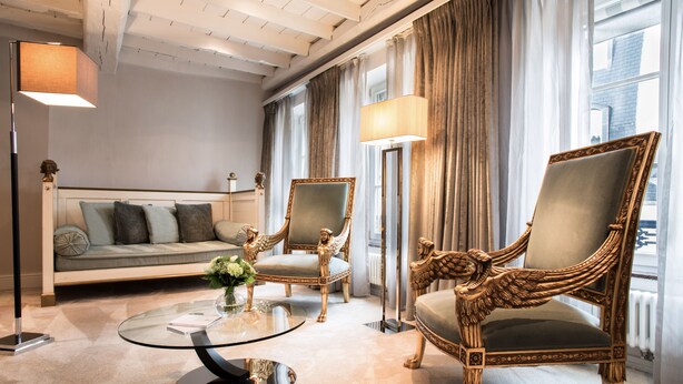 Ein luxuriöses Wohnzimmer mit einer Couch, zwei verzierten Sesseln, einem Glastisch und einer Stehlampe.