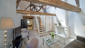 Amplia sala de estar con techo alto, vigas de madera a la vista, una escalera y una mesa de centro de vidrio con un florero.