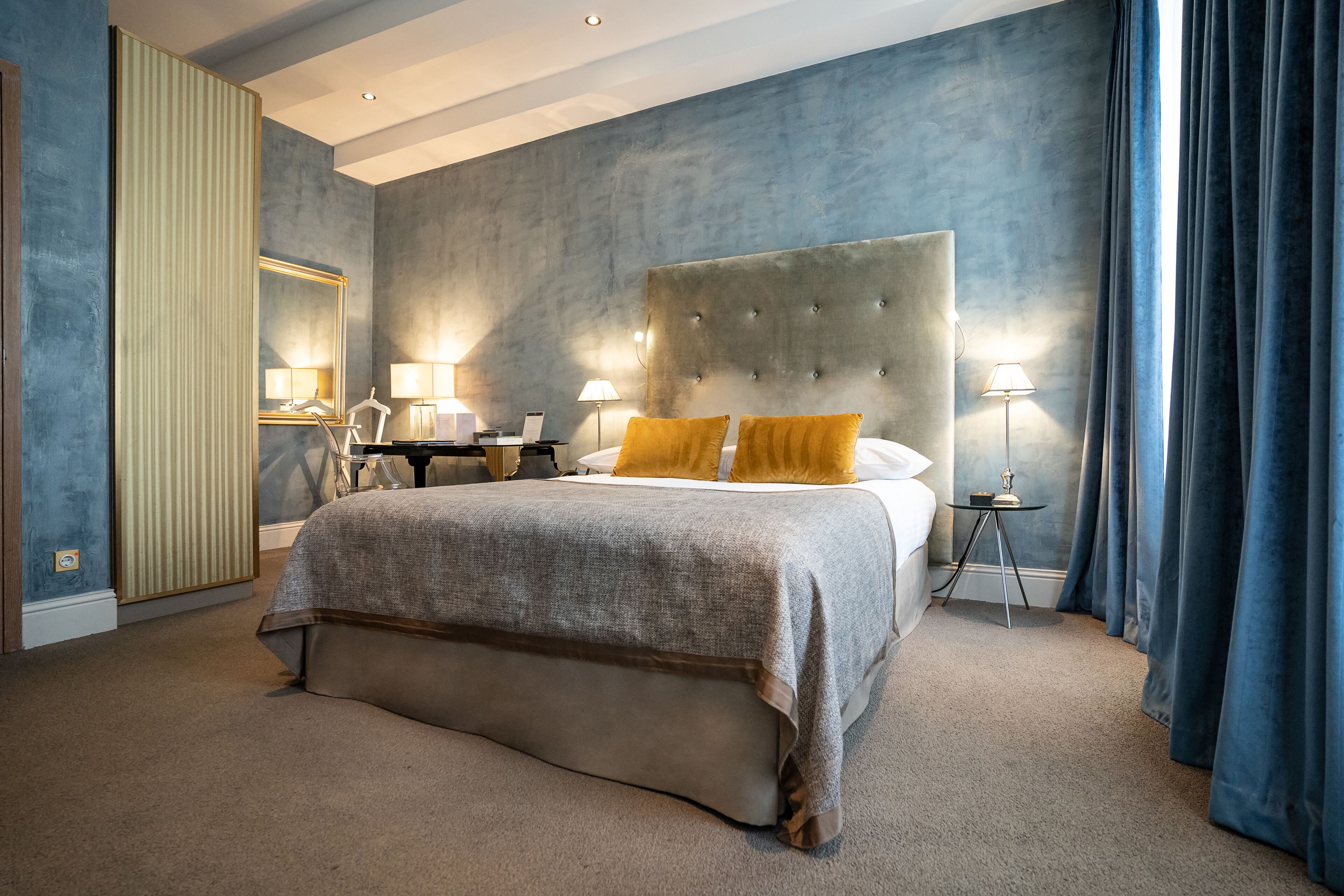 Ein modernes Hotelzimmer mit einem großen Bett, zwei Nachttischen, einem Spiegel und einem großen Fenster mit Vorhängen.