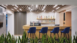 Un espace bar moderne avec un comptoir en bois, des chaises bleues et une variété de bouteilles d’alcool.