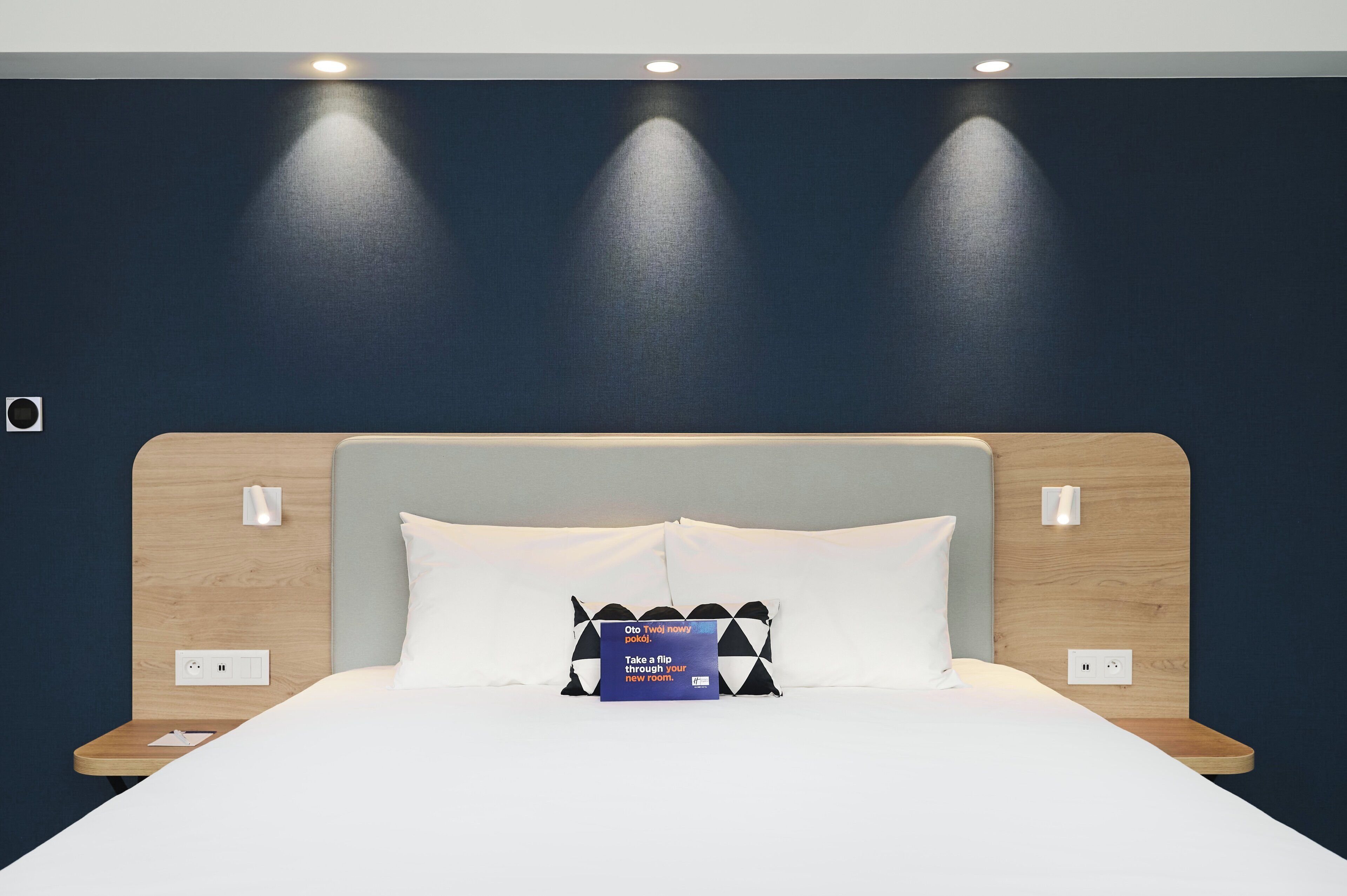 A modern hotel room with a large bed, two bedside tables, and a headboard with integrated lighting.