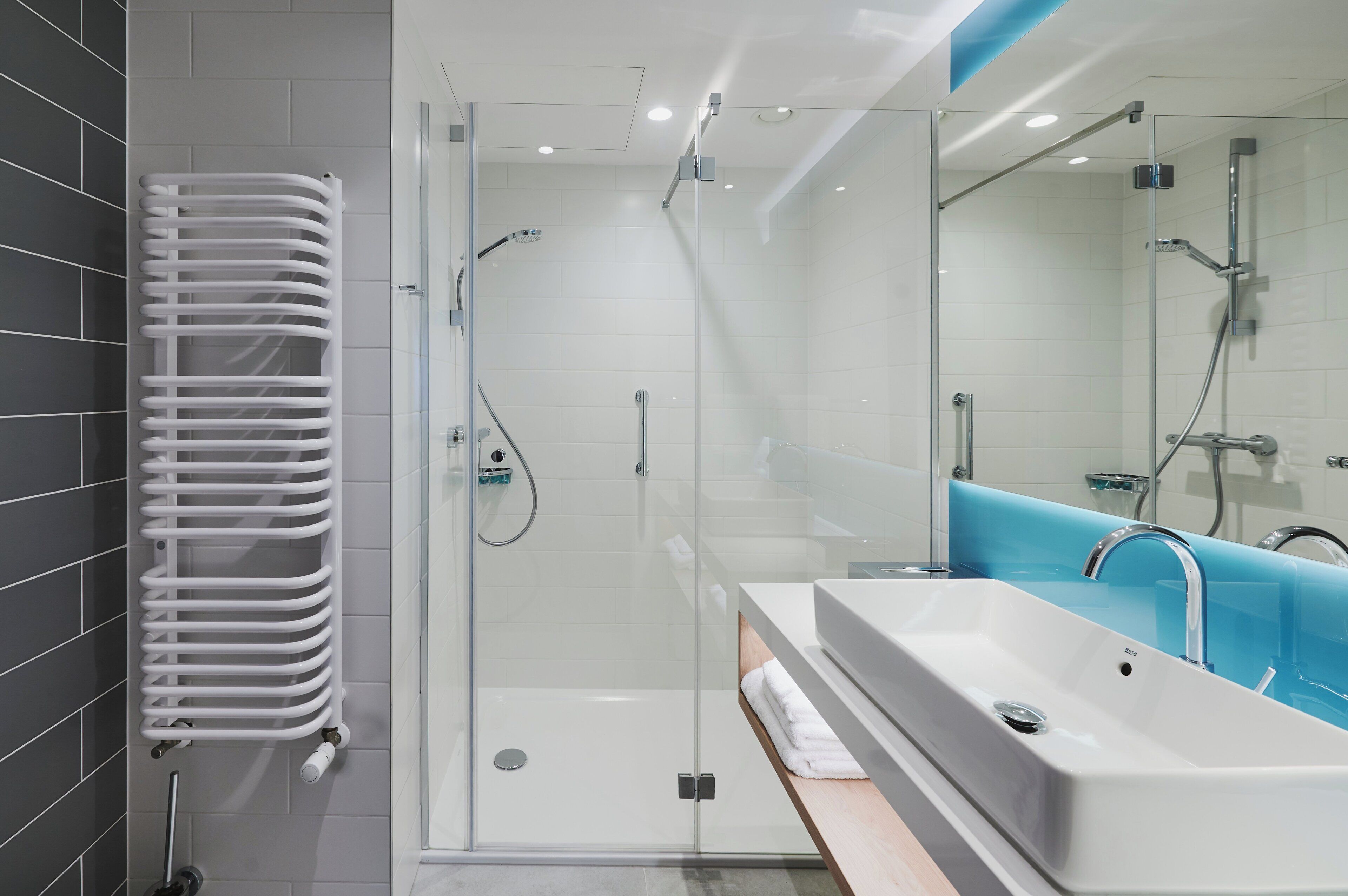 A modern bathroom with a glass-enclosed shower, a white bathtub, and a towel rack.