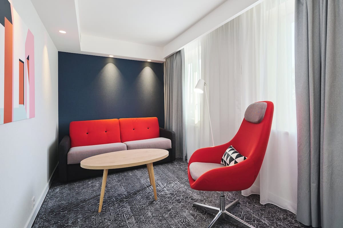 A modern hotel room with a red armchair, a grey sofa, and a round table.