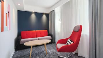A modern hotel room with a red armchair, a grey sofa, and a round table.