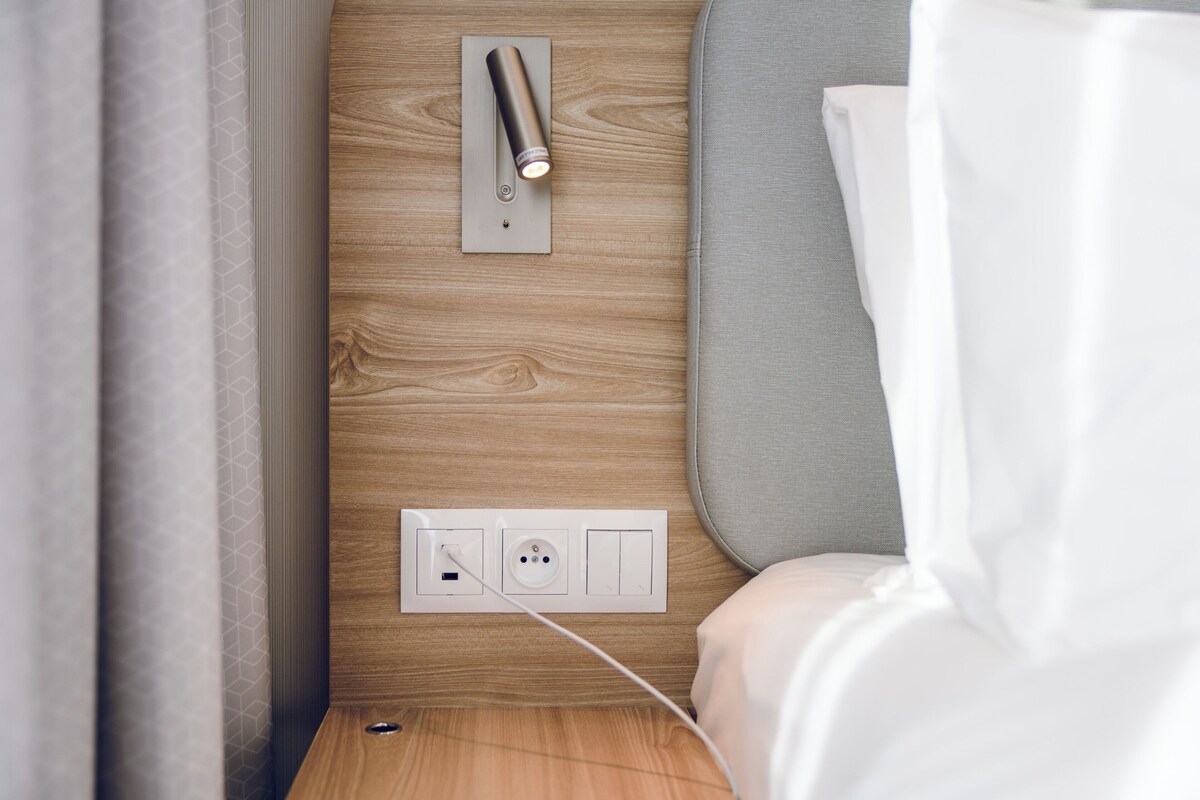 A modern bedroom with a wooden wall, a bedside table, a power outlet, and a lamp.