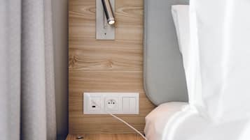 A modern bedroom with a wooden wall, a bedside table, a power outlet, and a lamp.