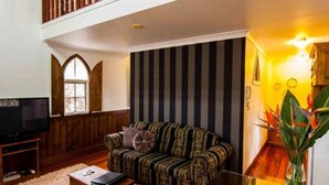Ein geräumiges Wohnzimmer mit hohen Decken, einer Holztreppe, einer gestreiften Wand und einem Fernseher auf einem Holzboden.