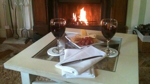 Ein Tisch mit weißem Serviet, Messer und zwei Gläsern Rotwein, vor einem Kaminfeuer.