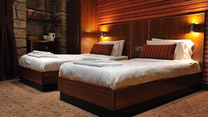 A hotel room with two beds, wooden headboards, and a stone accent wall. - The Commercial Hotel (Wishaw)