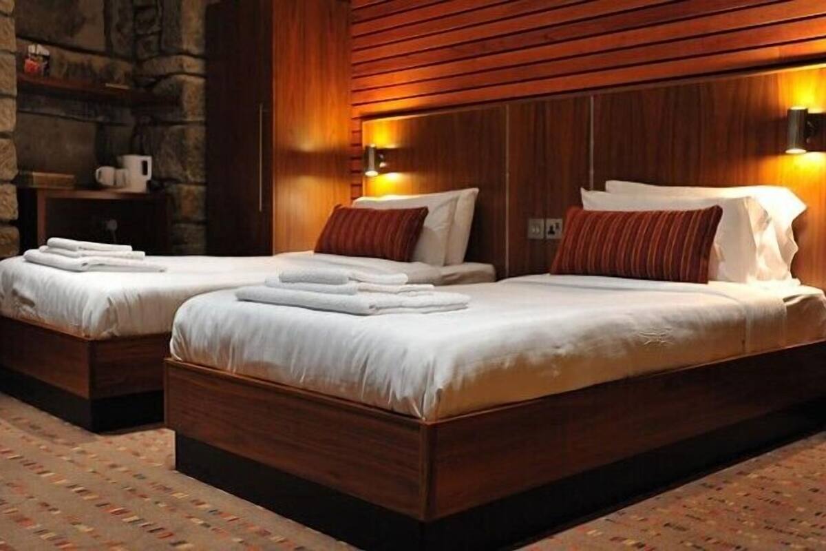 A hotel room with two beds, wooden headboards, and a stone accent wall.