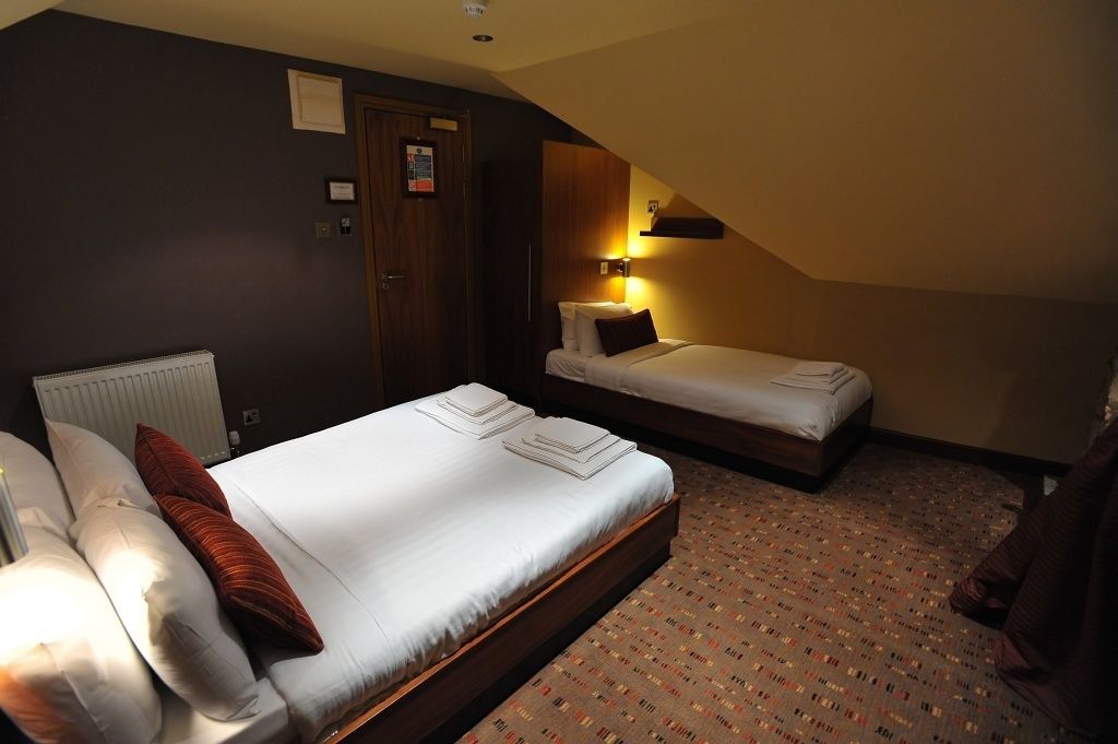 A hotel room with a large bed, a smaller bed, a nightstand, a lamp, and a door.