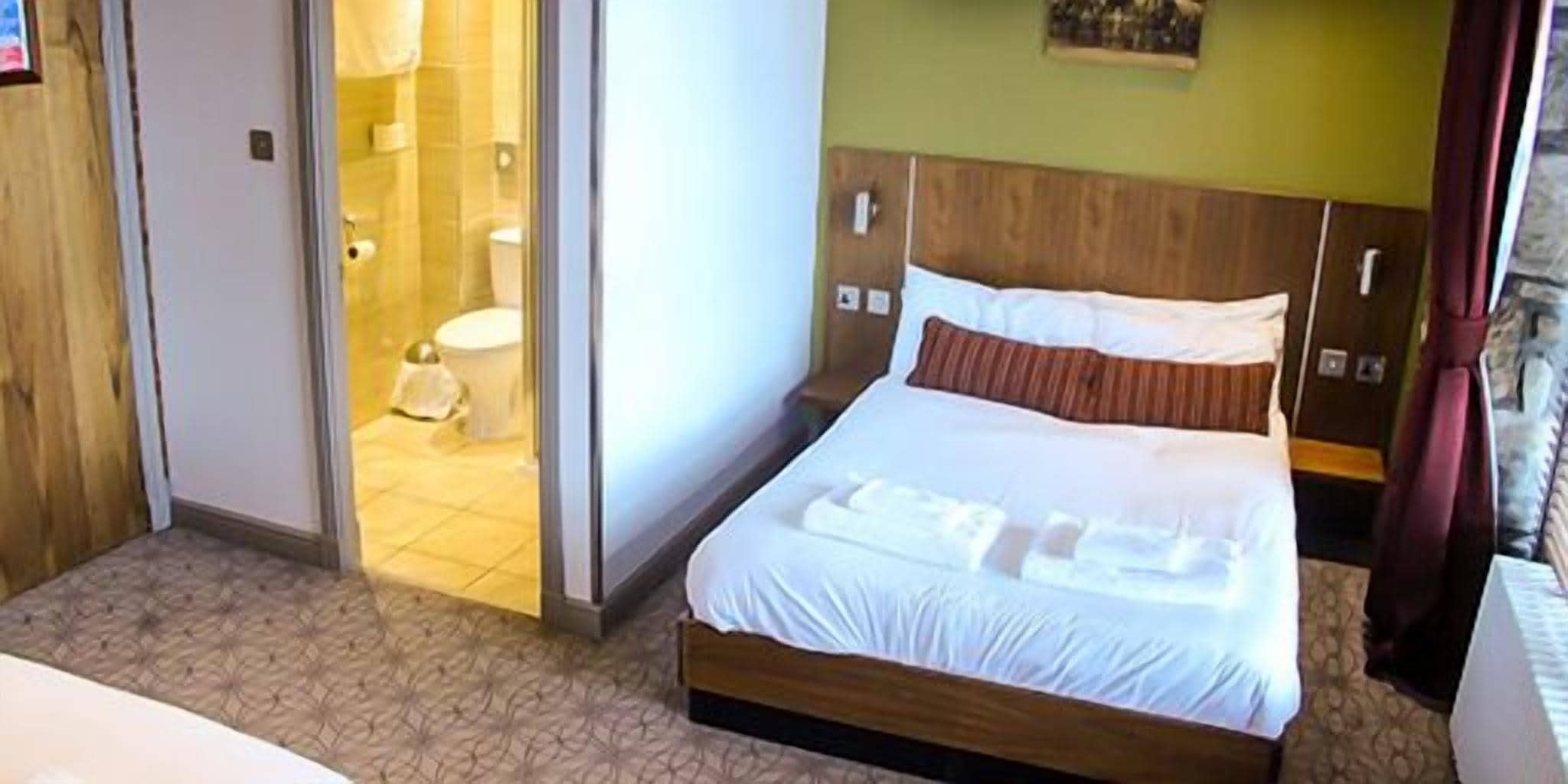 Ett hotellrum med en säng, ett badrum som syns genom en öppen dörr och en sänggavel i trä.