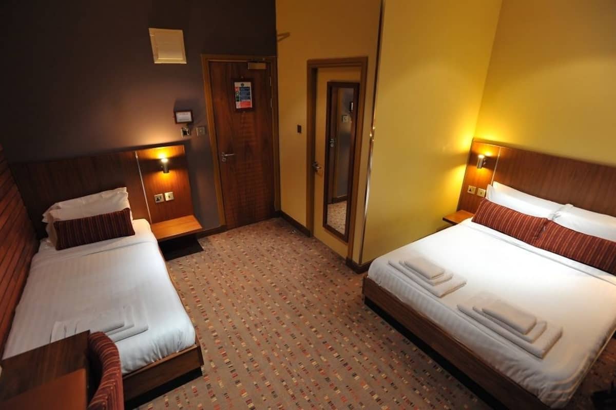 A hotel room with two beds, wooden headboards, and a patterned carpet.