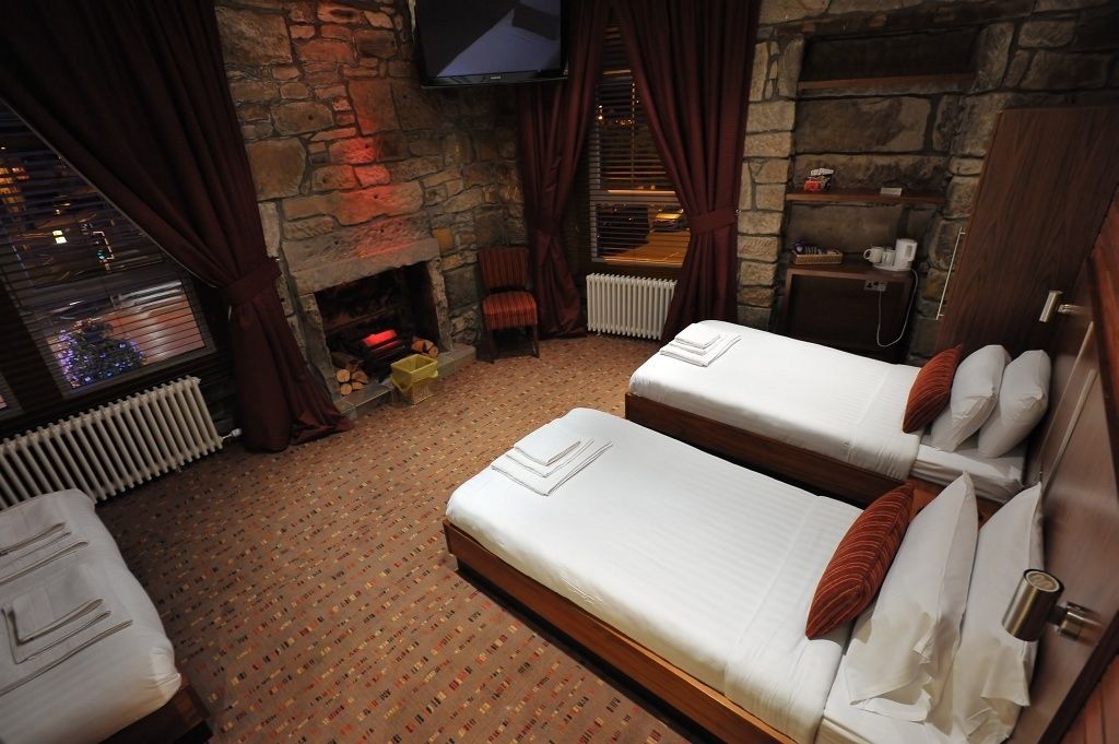 Habitación de hotel con dos camas, chimenea de piedra, televisión y vistas al exterior.