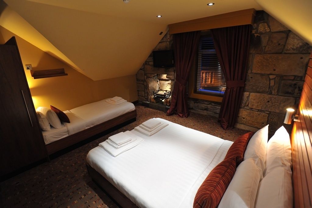 A bedroom with two beds, a stone wall, a fireplace, and a television.