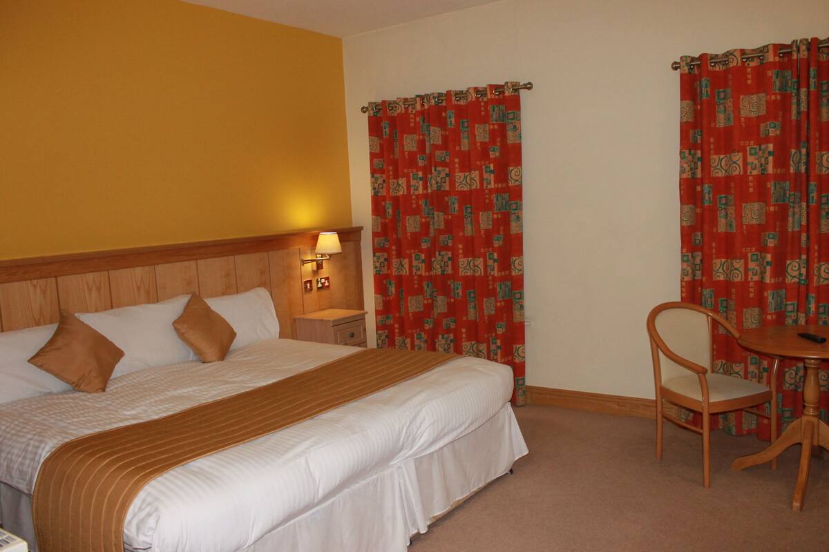 A hotel room with a bed, a nightstand, a lamp, a chair, and curtains.