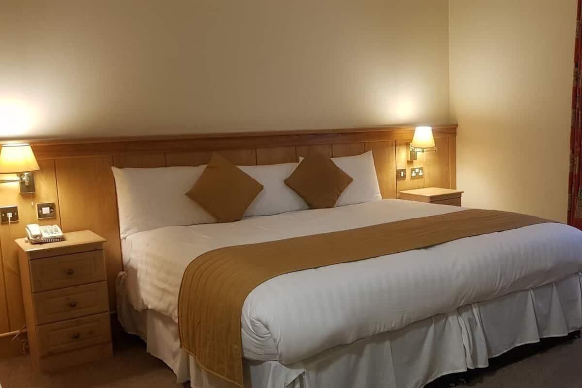 A neatly made bed with a wooden headboard, two bedside lamps, and a telephone on the nightstand.