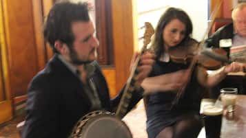 A group of people playing musical instruments in a room with wooden paneling and a patterned carpet.