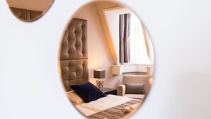 Quarto de hotel moderno com cabeceira estofada, luminária de cabeceira, cama com colcha listrada e janela com cortinas.