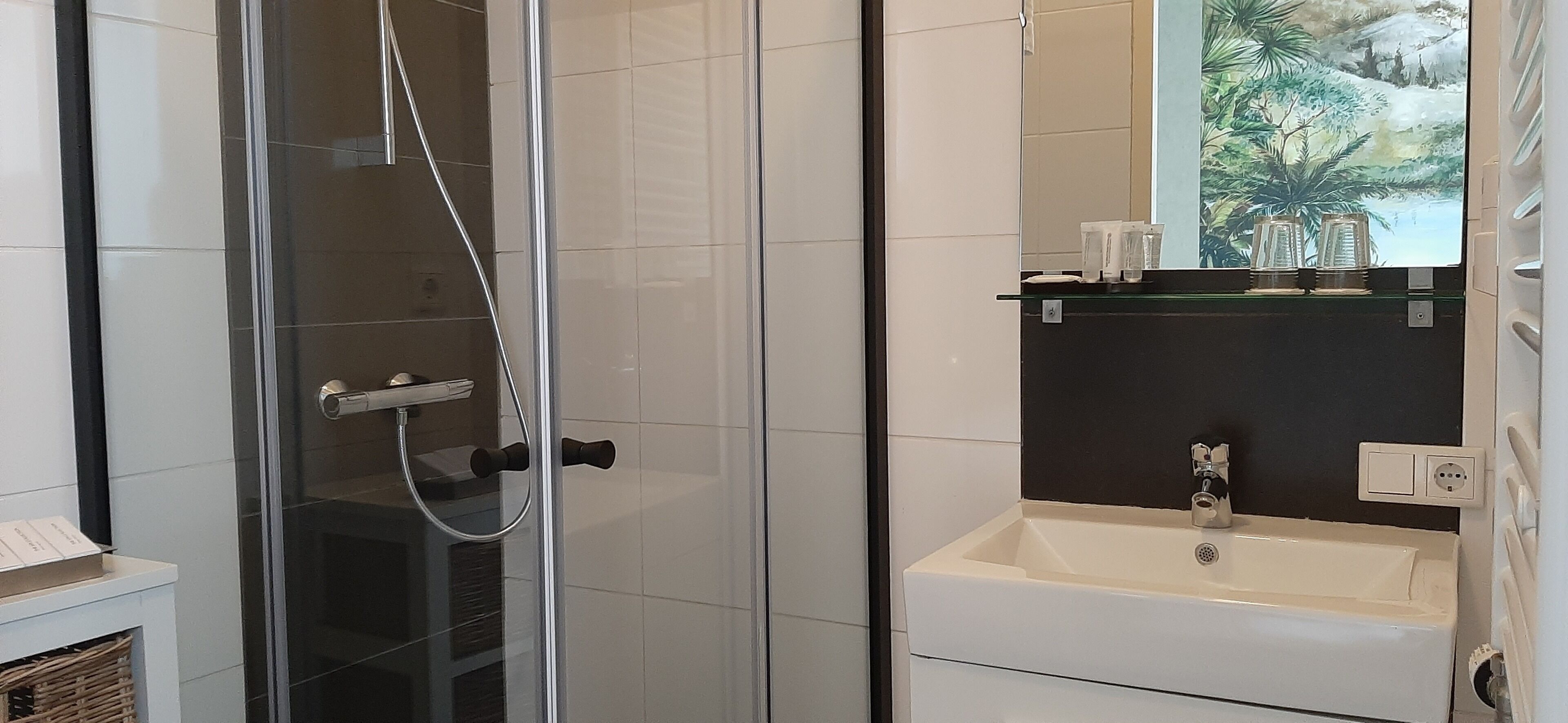 A modern bathroom with a glass shower enclosure, a white sink with a black countertop, and a mirror with a scenic view.