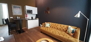 A living room with a sofa, a coffee table, a dining area with a table and chairs, a kitchen with a microwave, and a lamp. - Hotel Zilt (Vlissingen)