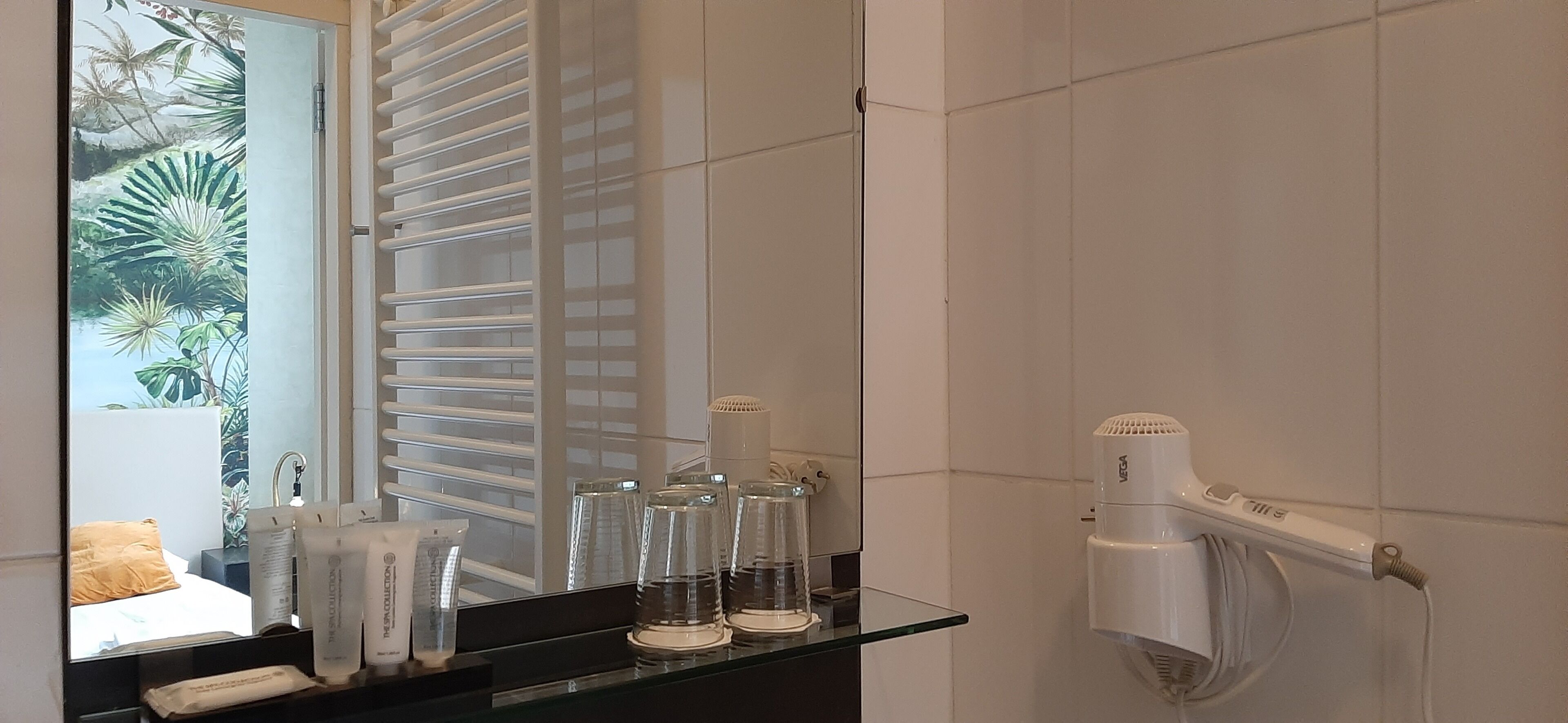 A bathroom with a glass shower enclosure, a white hairdryer mounted on the wall, and toiletries on a black countertop.
