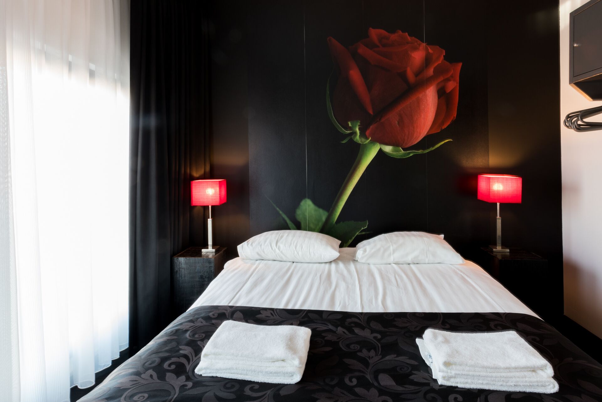 A hotel room with a large bed, two bedside lamps, and a wall-mounted rose decoration.
