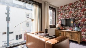 Uma sala de estar moderna com um sofá de couro, um armário de madeira, uma televisão de tela plana e uma janela grande com cortinas.