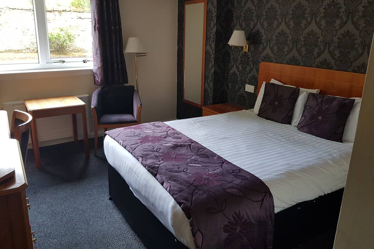 A hotel room with a bed, a desk, a chair, a lamp, and a mirror.