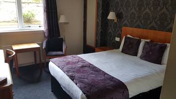 Ein Hotelzimmer mit Bett, Schreibtisch, Stuhl, Lampe und Spiegel.