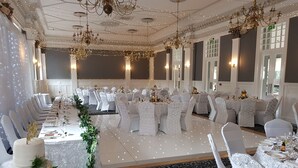 Un salón de banquetes con manteles blancos, sillas y un pastel de varios niveles como decoración central.