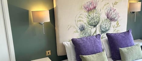 Habitación de hotel con una cama grande, dos lámparas fijadas a la pared y un cabecero decorativo.