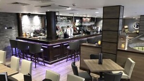 Un área de bar moderna con barra, taburetes y una zona de estar con mesas y sillas.