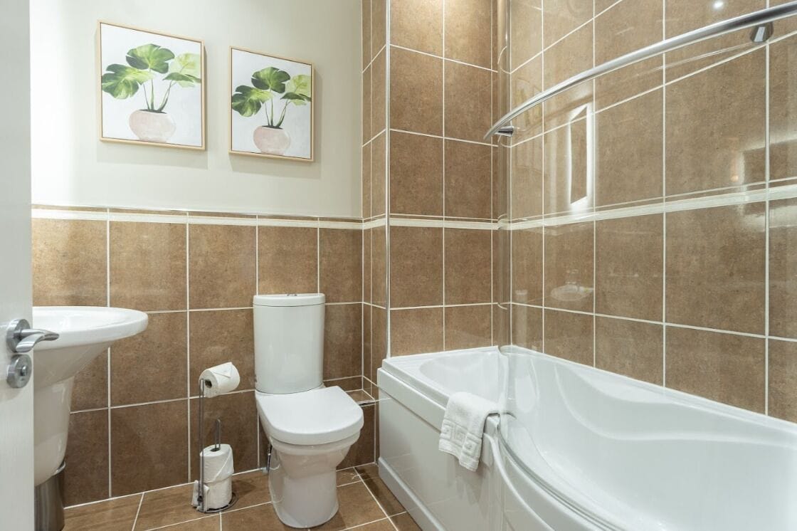 Un baño con bañera, inodoro, lavamanos y dos cuadros de plantas enmarcados en la pared.
