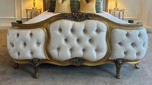 Una cama grande y ornamentada con cabecera y piecera acolchados, flanqueada por dos mesitas de noche con lámparas.