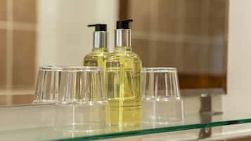 Un baño con un estante de vidrio que contiene dos botellas de jabón líquido y varios vasos de cristal.