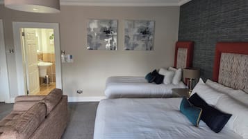 A hotel room with two beds, a sofa, a bathroom, and abstract wall art.