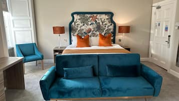 A hotel room with a bed, a blue sofa, a chair, a nightstand, and a door.