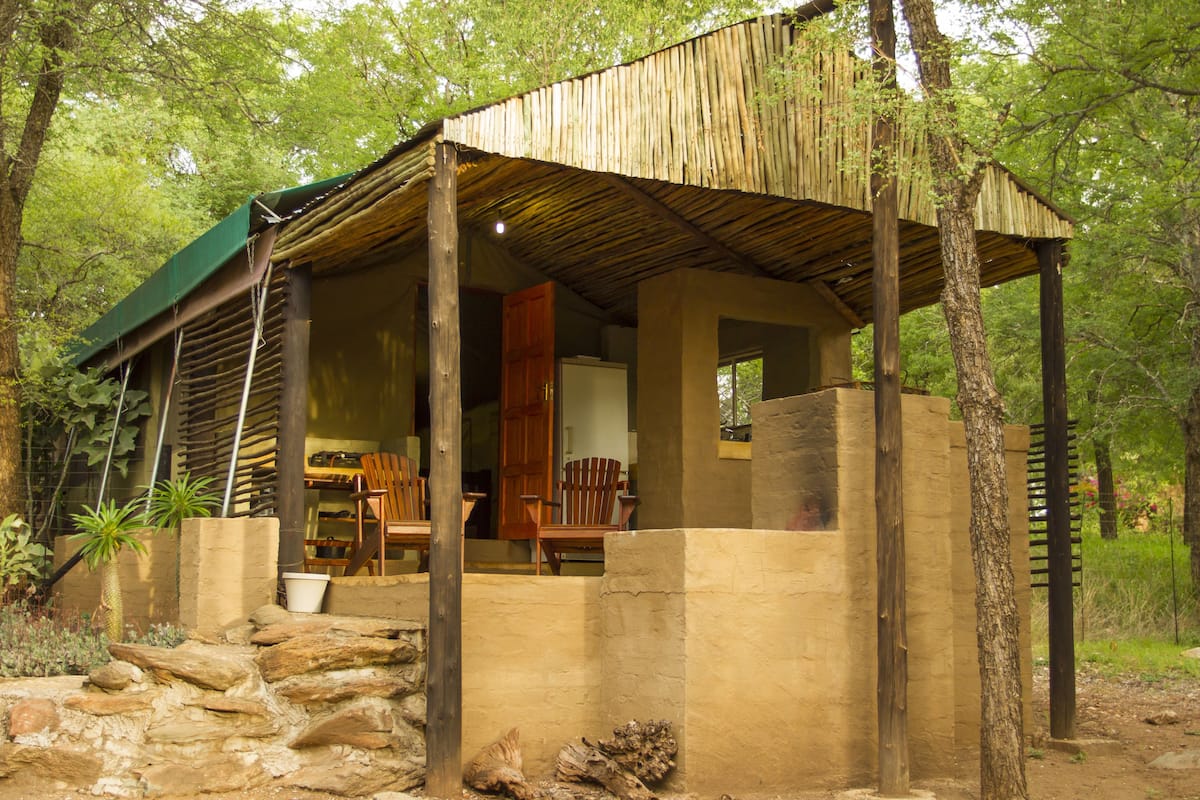Ein rustikales Holzgebäude mit überdachter Veranda, Steinmauern und einem sichtbaren Stuhl.