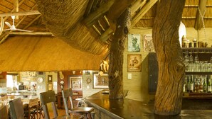 Un coin bar rustique avec des chaises en bois, un plafond en chaume et un comptoir en pierre.