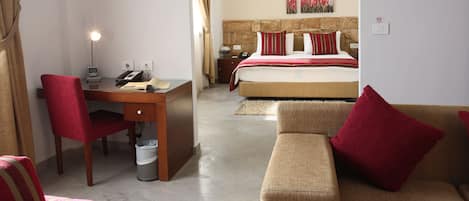 Habitación de hotel con cama, escritorio con teléfono, silla, sofá y cubo de basura.