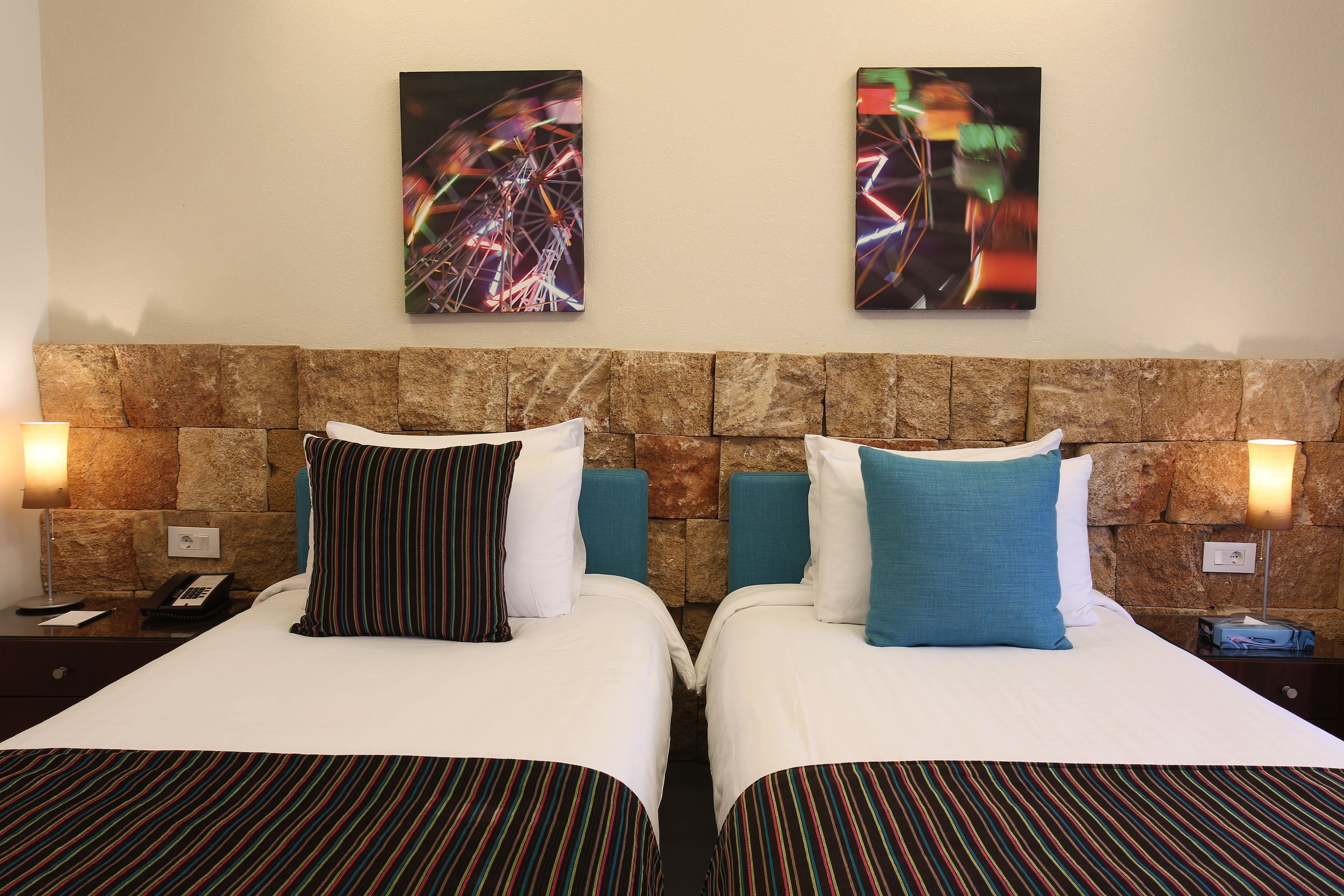 A hotel room with two beds, each with striped bedding, a stone headboard, and artwork on the wall.